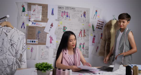 Teacher woman helping a fashion student girl looking a sketch of women's clothing in studio alt
