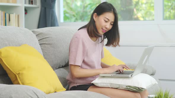 Young business Asian woman working on laptop checking social media while lying on the sofa.