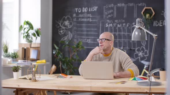 Bald Businessman in Glasses Working on Laptop in Office alt