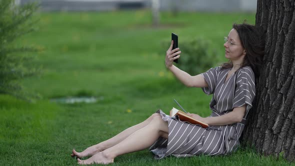 Adult Brunette Woman with Book and Smartphone is Resting in Park at Summer Day alt