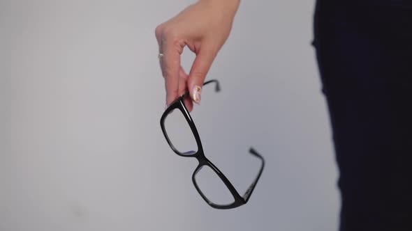 female hand is holding model of eyeglasses with black rim on a gray background alt