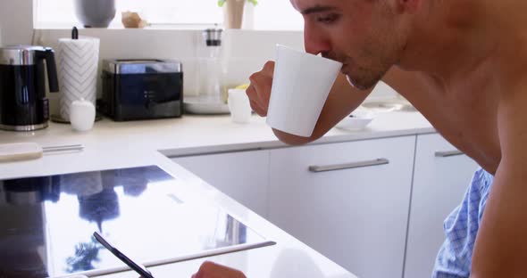 Young man using mobile phone and drinking coffee in kitchen at home 4k