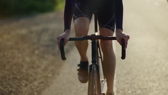Cropped Front View of a Male Cyclist Rides Bicycle Along Track in the Morning Slow Motion alt