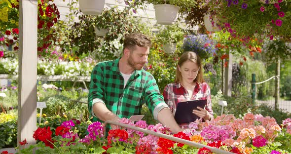 Two Gardeners Doing Paperwork Between Plants alt