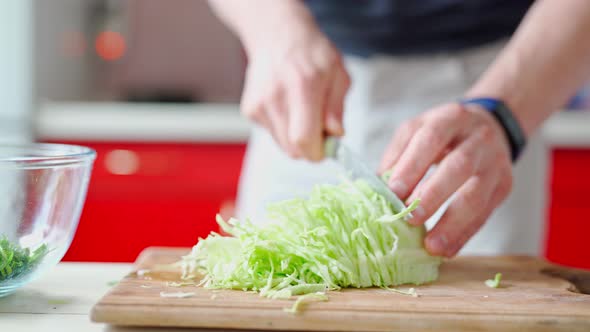 Male Hands with Knife Cuts Fresh Cabbage on Wooden Cutboard on White Kitchen alt