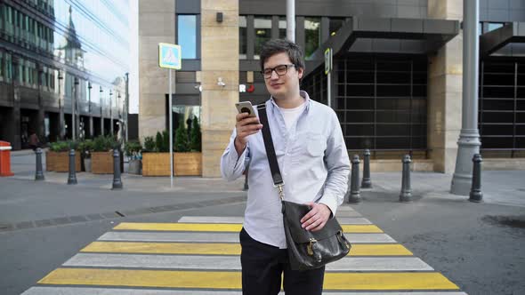 Middle Shot of Man in Eyeglasses and Blue Shirt Crossing the Road with a Phone