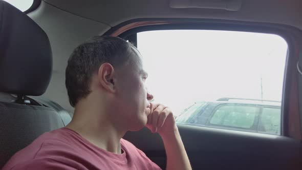 A Man Rides in the Passenger Seat of a Car and Looks at City Life Through a Dirty Car Window alt