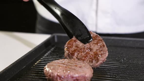 meat for burger is fried in grill pan in kitchen. cook turns burger over spatula alt