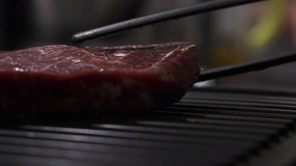 Close Up Red Beef Steak Is Placed on Home Grill Using Special Plastic Black Tongs alt