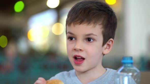 Boy with Medical Mask Eats a Burger with Cutlet Sitting in Restaurant