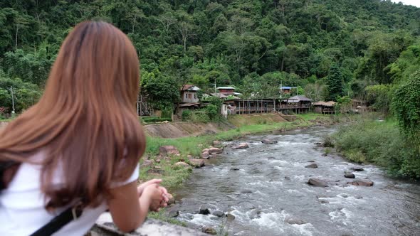 Blurred rear view of a woman looking at the river flowing trough rural village in valley, Thailand