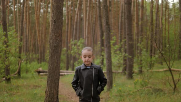 The Little Girl Runs Along the Path Road in the Pine Forest. Dressed in the Leather Jacket