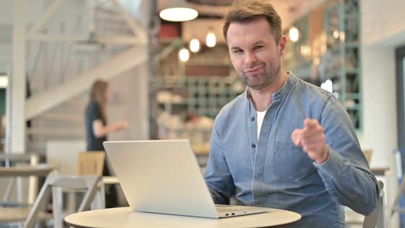 Casual Man with Laptop Pointing at Camera in Cafe alt