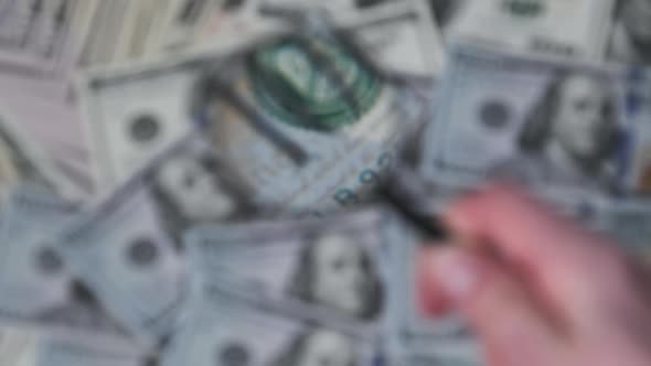 Lot of One Hundred Dollars Bills Inspecting Under Magnifying Glass alt