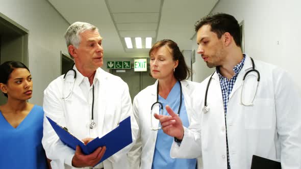 Doctors and nurse discussing over medical report while walking in corridor alt