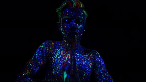 Young Man Painted in Fluorescent Paint Glow in Dark Dancing Performing Hand Movements on Dark alt