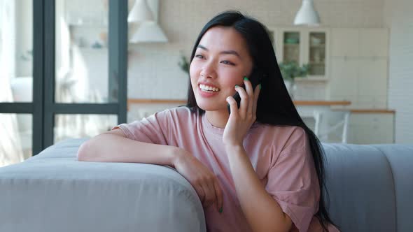 Beautiful and Friendly Young Asian Ethnicity Woman in Pink Tshirt Sitting on the Sofa and Leaning alt