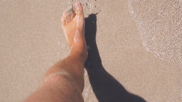 Closeup of Men's Legs Walking on a Sandy Beach Next to the Sea alt