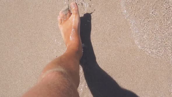 Closeup of Men's Legs Walking on a Sandy Beach Next to the Sea