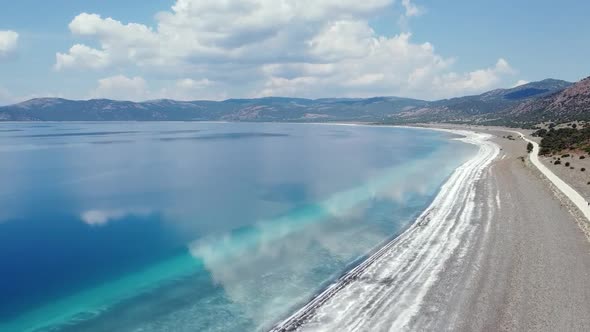 Quadcopter Flight Between Blue Water and White Beach Against the Backdrop of Mountains