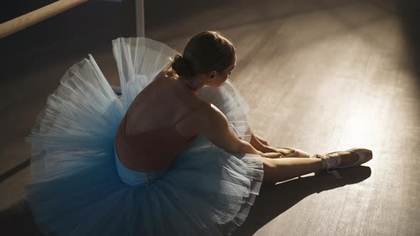 Wide Shot of Confident Slim Ballerina in Blue Tutu Putting on Beige Pointes Sitting on Floor in alt
