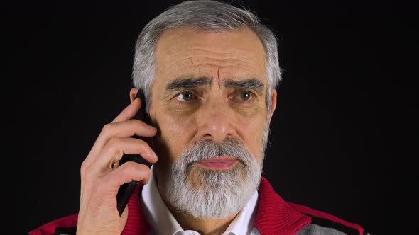 An Elderly Man Talks on a Smartphone - Face Closeup - Black Screen Studio alt