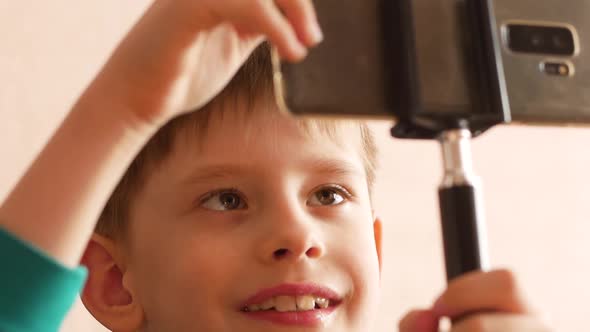 Caucasian boy 6-7 years old makes a selfie photo using a smartphone on a selfie stick. alt