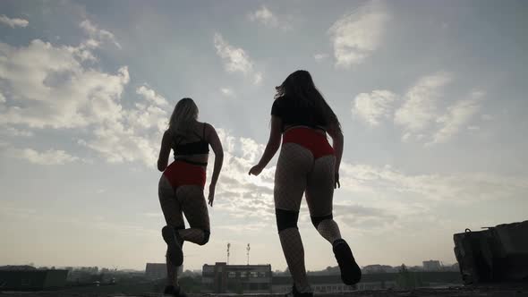 Two Girls Dance Twerk on the Roof of an Abandoned Building. Girls in Red Shorts and Checkered Tights