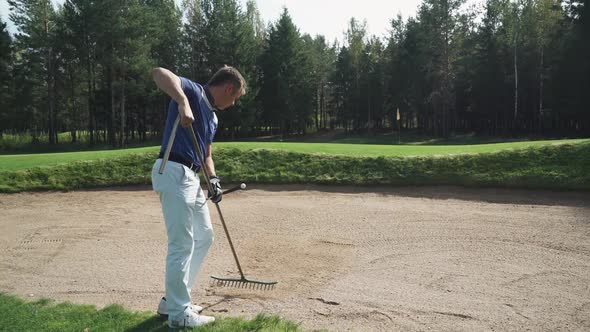 Summer Day Man Playing Golf Golfer Prepares the Ground Clear the Sand with a Rake alt