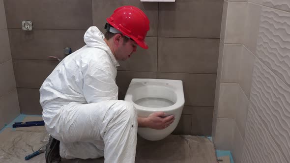 Professional Worker Man Hanging Heavy Toilet Bowl Pan in New Modern Bathroom