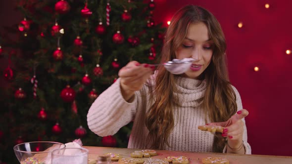 Beautiful Woman Making Xmas Cookies Sprinkling Gingerbread with Sugar Powder