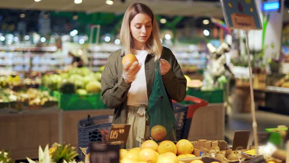 young woman chooses and picks in eco bag vegetables or fruits Oranges  alt