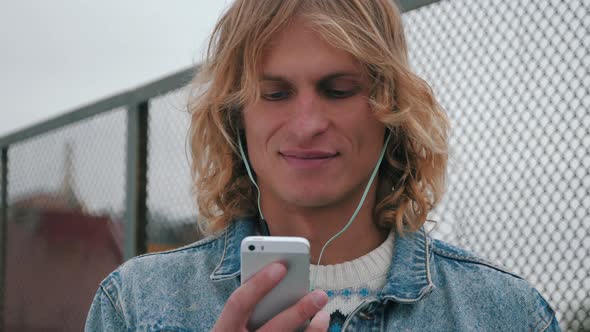Smiling handsome young man listening music from his smartphone in blue headphones
