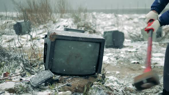 Person Breaks a TV with a Hammer at a Dump. Man with a Hammer Shatters the TV Screen. alt