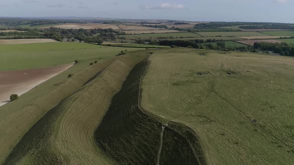 Aerial tracking down between the outer ramparts of the iron age hill fort of Maiden Castle. Sheep gr alt
