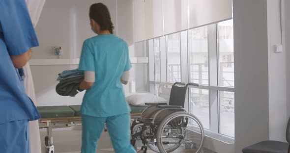 Young Nurse in Blue Uniform Gloves and Mask Changing Bedsheets of Hospital Bed in the Hospital Ward alt