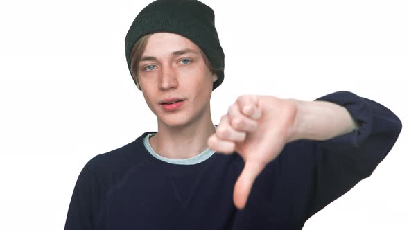 Portrait of Young Disappointed Man in Hat Being Upset Showing Thumb Down Expressing Dislike Over alt