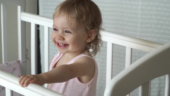 Portrait of Girl with Curly Hair Smiles and Laughs in White Crib