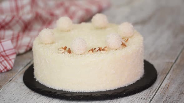 Female Hands Sprinkle Coconut Mousse Cake with Almonds