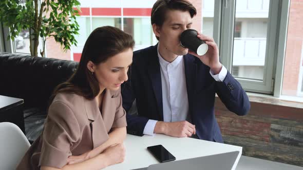 Young Man and Woman Discuss. Man Shows Details on the Screen Woman Listens Holding Cup  alt