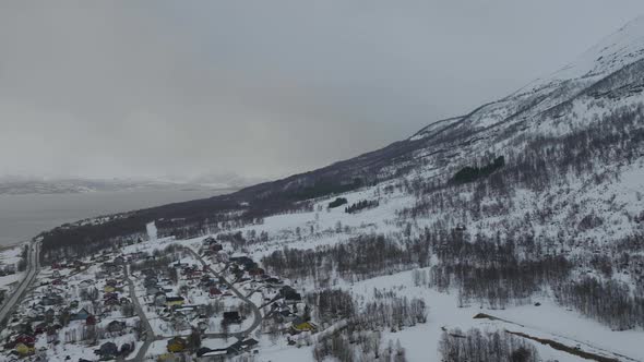 Olderdalen town nestled at foot of mountain, freezing snowy landscape; aerial alt