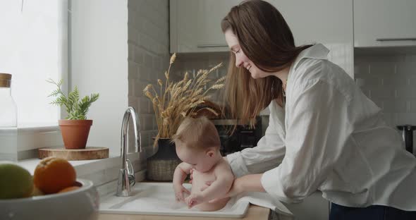 Cute Baby Girl Takes a Bath in the Kitchen Sink Having Fun in Water