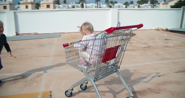 Kids Having Fun Playing with Supermarket Sopping Cart in Parking Outdoors alt