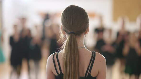 Back View Closeup of Caucasian Girl Standing in Dancing School with Blurred Children Clapping at alt