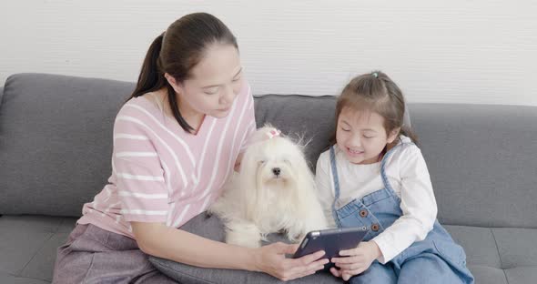 mother and daughter playing with white dog on sofa 1