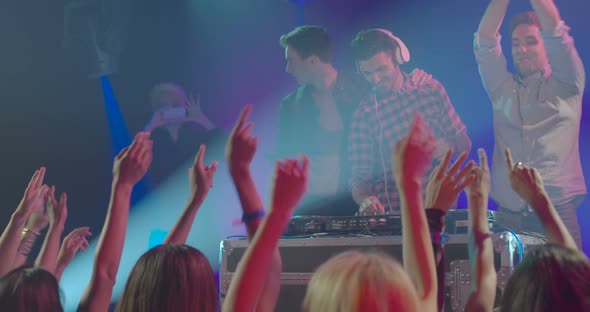 Man operating DJ machine and his friends dancing on music in nightclub