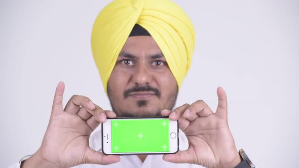 Face of Happy Bearded Indian Sikh Businessman Showing Phone alt