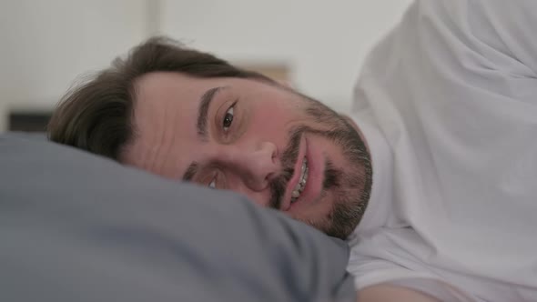 Portrait of Young Man Talking on Video Call While Laying in Bed alt
