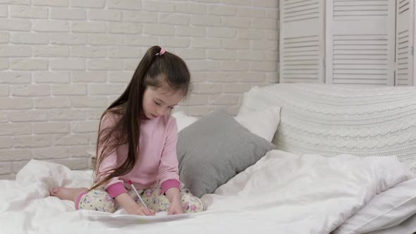 Cute Little Girl Drawing Pictures While Lying on Bed
