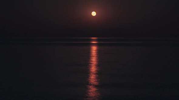 The Full Red Moon Shines Brightly in the Sky on a Dark Night Over the Calm Sea